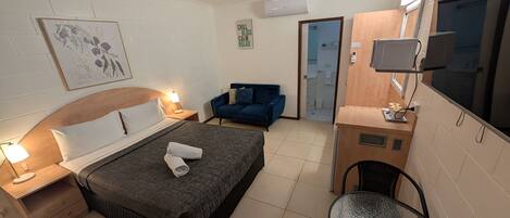 Een moderne hotelkamer met een bed, een bureau, een stoel, een televisie en een badkamer die door een geopende deur zichtbaar is.