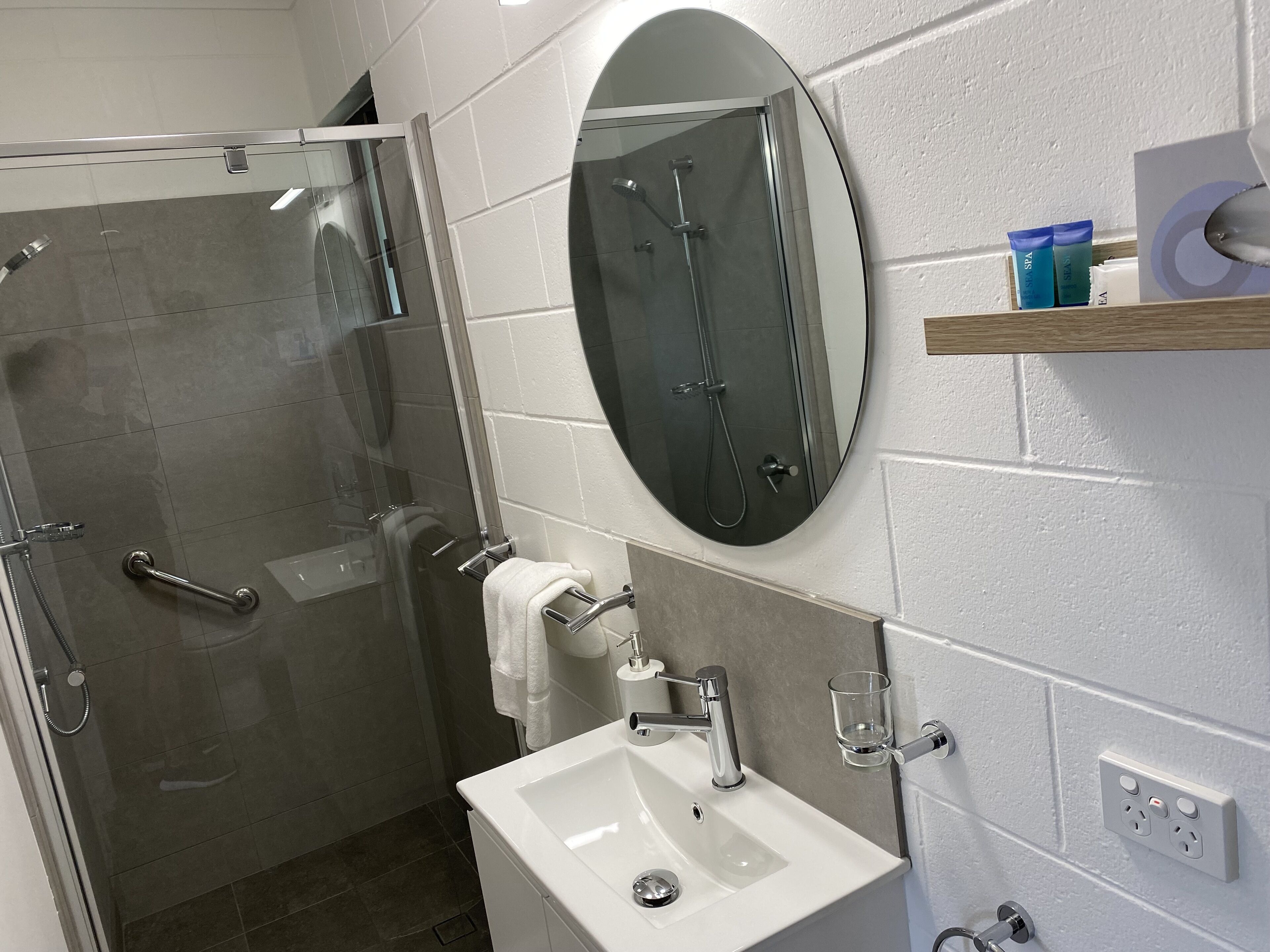A modern bathroom with a glass-enclosed shower, a white sink, and a round mirror.