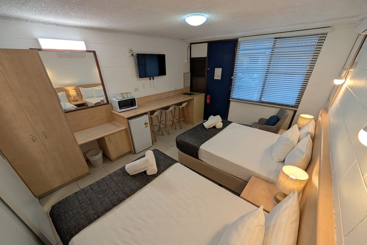 A hotel room with two beds, a desk, a microwave, and a TV.