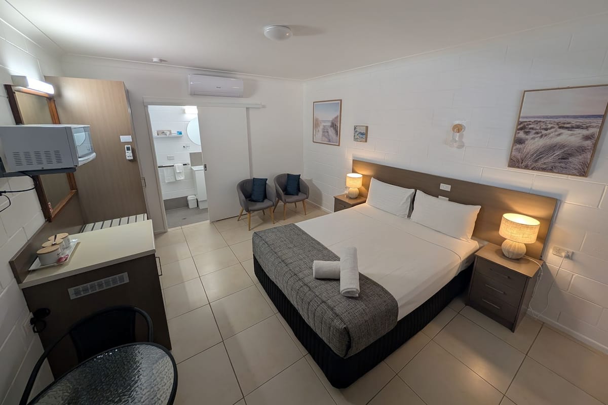 A hotel room with a bed, bedside tables, a desk, a chair, and a television.