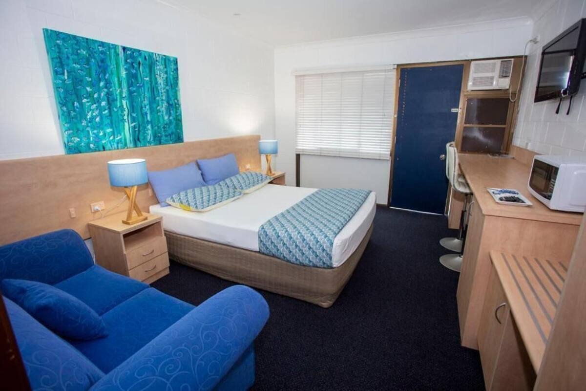 A hotel room with a bed, a desk, a chair, a TV, and a painting on the wall.