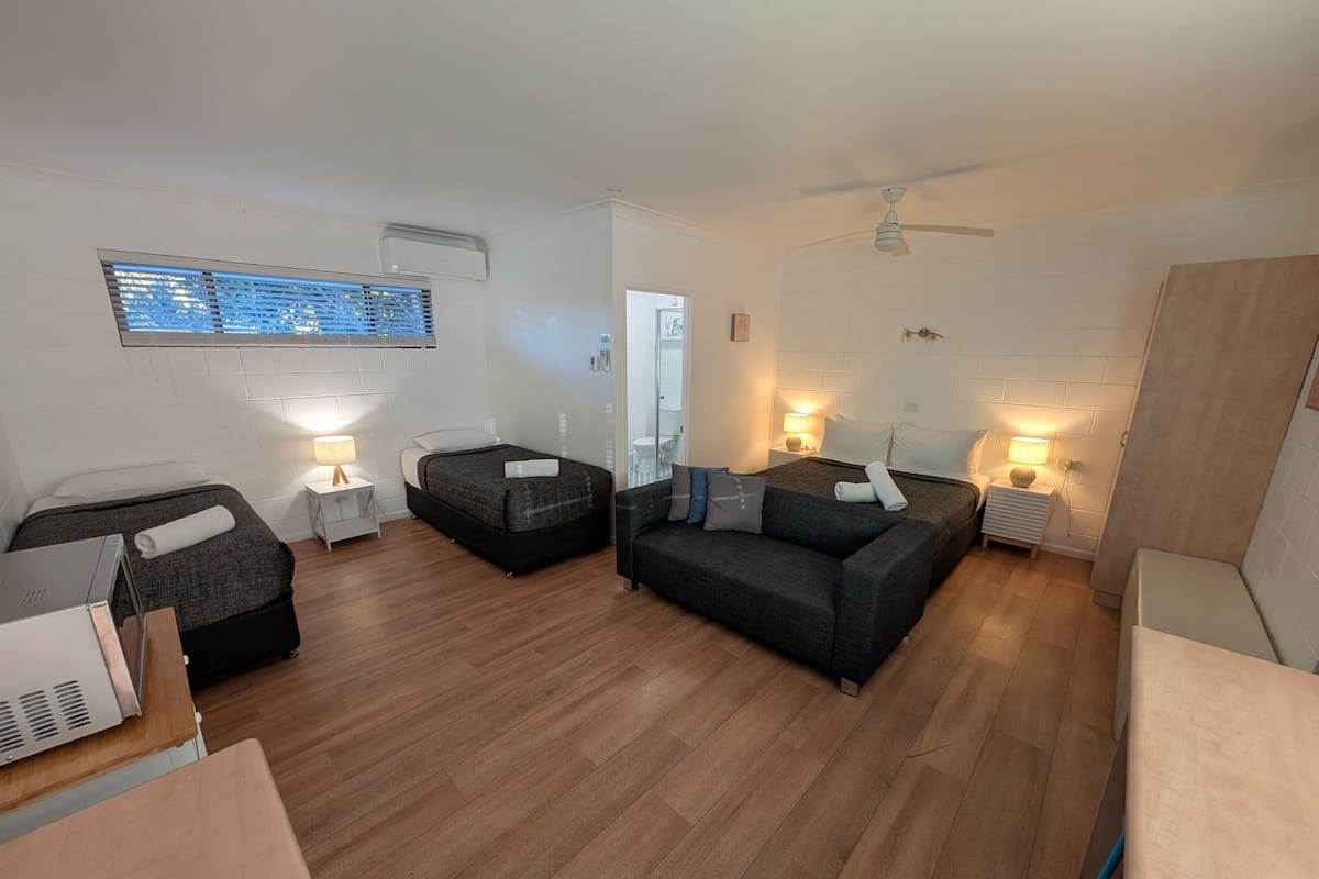 A modern, well-lit room with a bed, two sofas, a small table, and a ceiling fan.