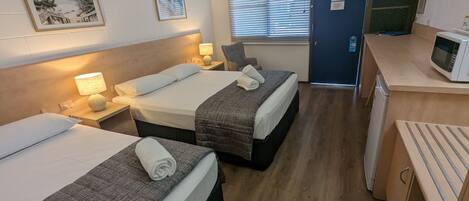 A hotel room with two beds, a desk with a microwave, and a window with blinds.