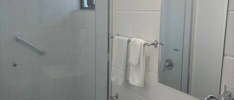 Un baño moderno con cabina de ducha de vidrio, un lavabo blanco con grifo cromado y un espejo con toallero.