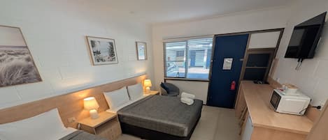 A hotel room with two beds, a desk with a microwave, a chair, and a TV on the wall.
