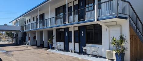 A two-story motel with a covered front porch, outdoor seating, and a small parking area.
