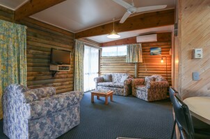 Interior de una cabaña de troncos con un sofá, una mesa de centro, un ventilador de techo y un televisor montado.