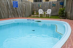 A swimming pool with a depth of 1.6 meters, surrounded by a wooden fence, two white chairs, and a small garden area with plants and a bird bath. - Lazy Acre Log Cabins (Lakes Entrance)