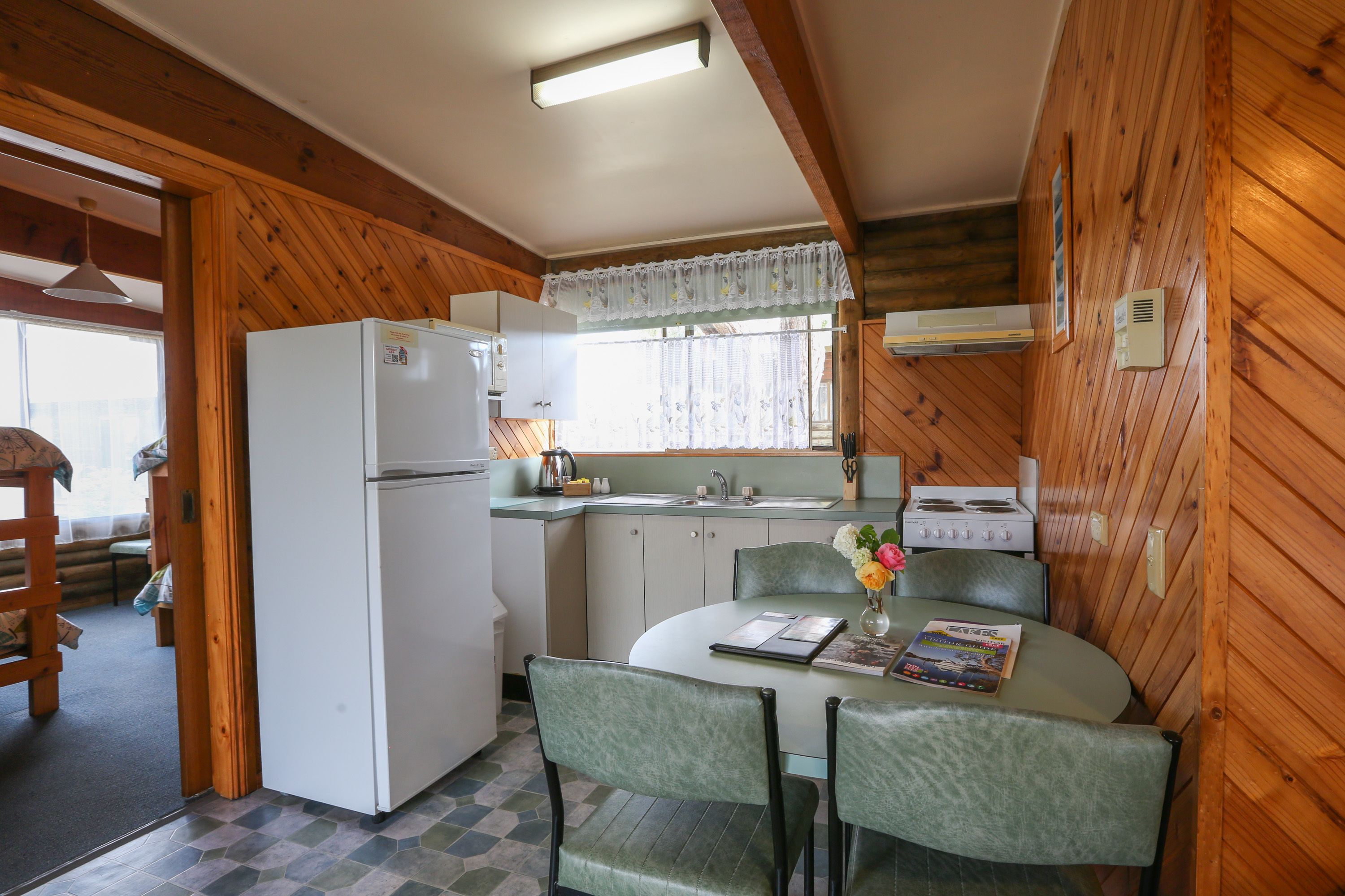 A compact kitchen with a refrigerator, stove, sink, and dining area with chairs and a table.
