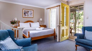 A bedroom with a bed, two bedside tables, a nightstand, a chair, a sofa, and a door leading to a balcony. - Honeysuckle Cottages Stanthorpe (Applethorpe)
