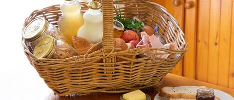 Een rieten mand met etenswaren zoals brood, boter en jam, op een houten tafel geplaatst.