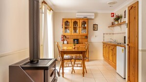 A compact kitchen with wooden cabinets, a dining table with chairs, a stove, and a refrigerator. - Honeysuckle Cottages Stanthorpe (Applethorpe)