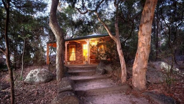 A rustic cabin with a stone staircase leading to a wooden door, surrounded by trees and rocks. - Honeysuckle Cottages Stanthorpe (Applethorpe)