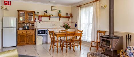 A cozy kitchen with wooden cabinets, a dining table, chairs, a microwave, a refrigerator, a fireplace, and a fire blanket sign on the wall.