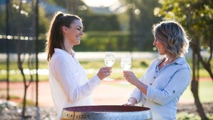 Two people standing by a wooden barrel outdoors.