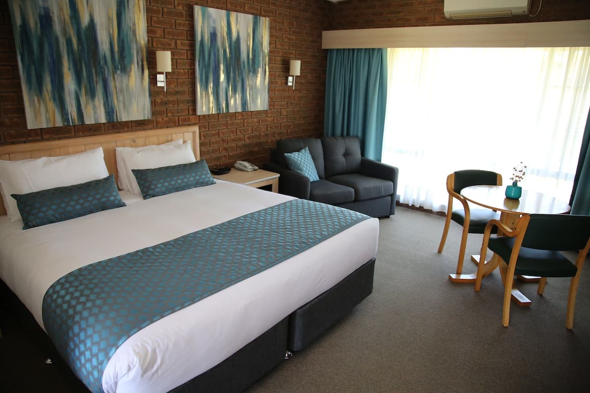 Ein Hotelzimmer mit einem großen Bett, einem grauen Sessel, einem Holztisch und zwei Wandleuchten.