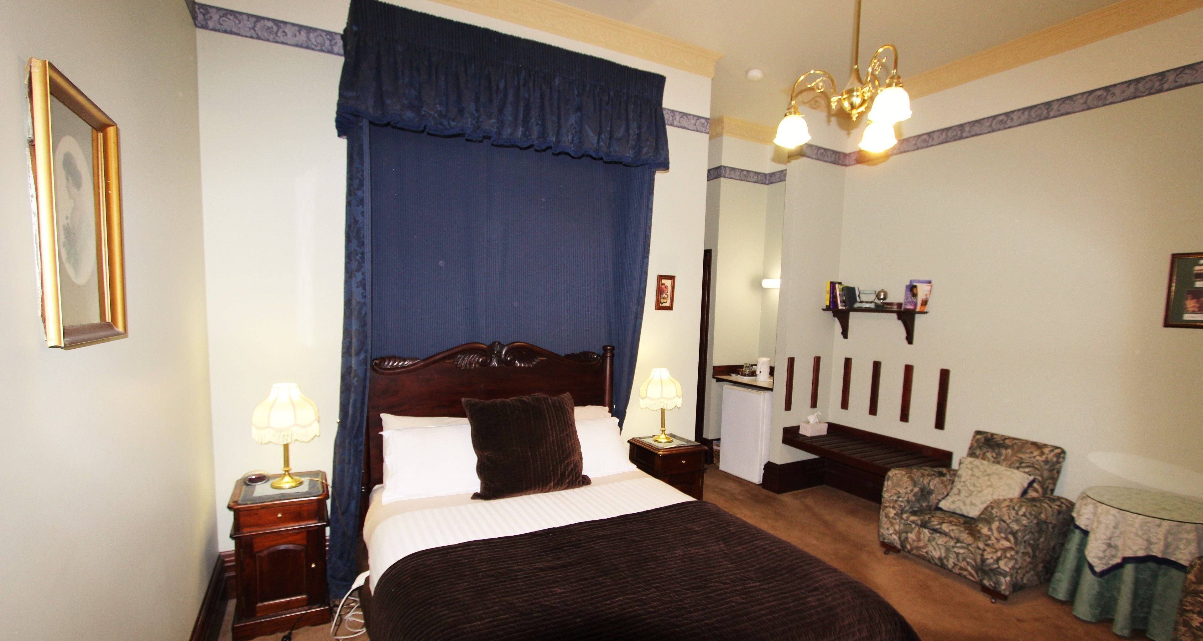 A hotel room with a large bed, a nightstand, a chair, a small table, and a mirror.