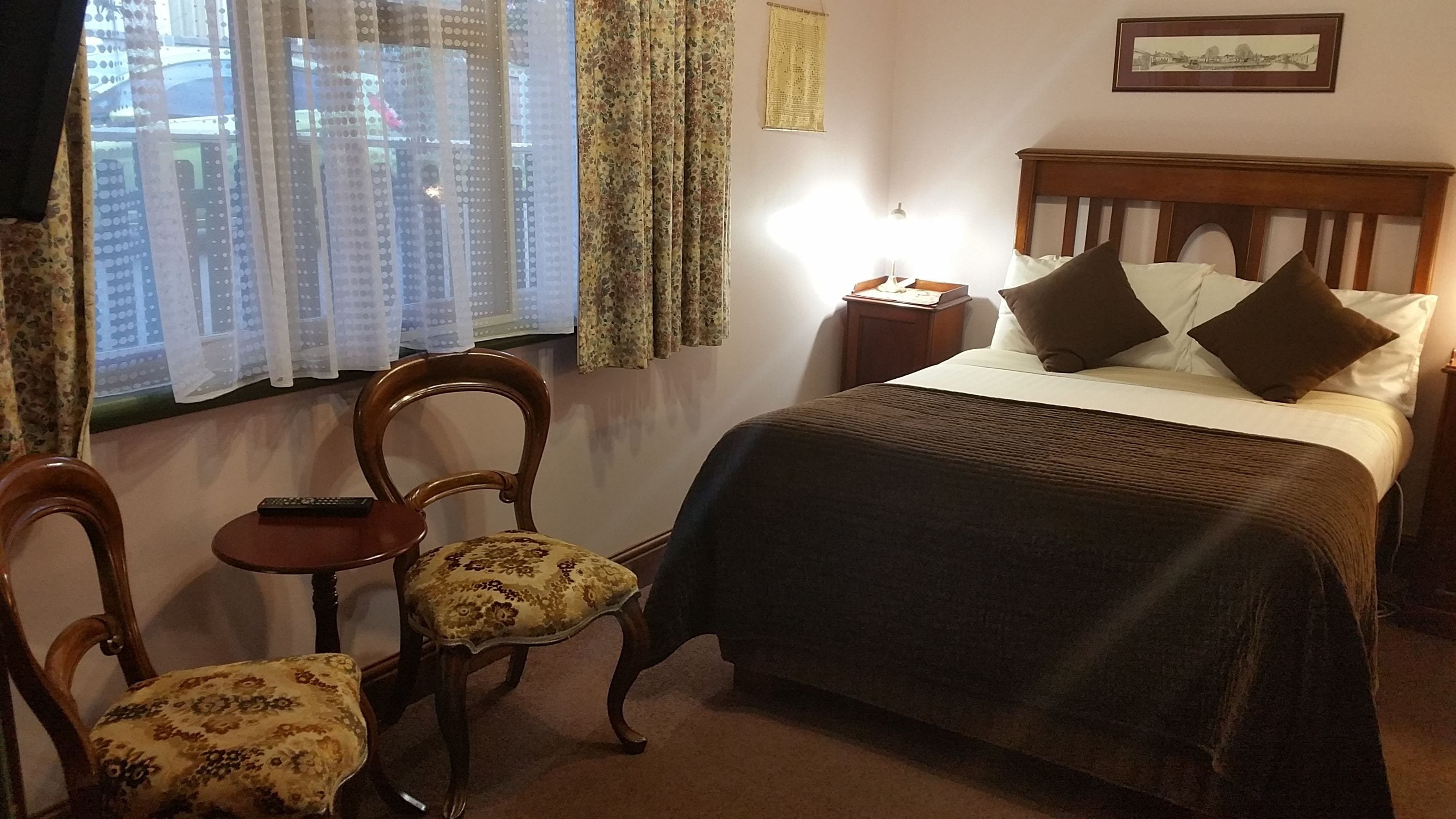 Un dormitorio con cama de madera, dos sillas, una mesita de noche y una ventana con cortinas.