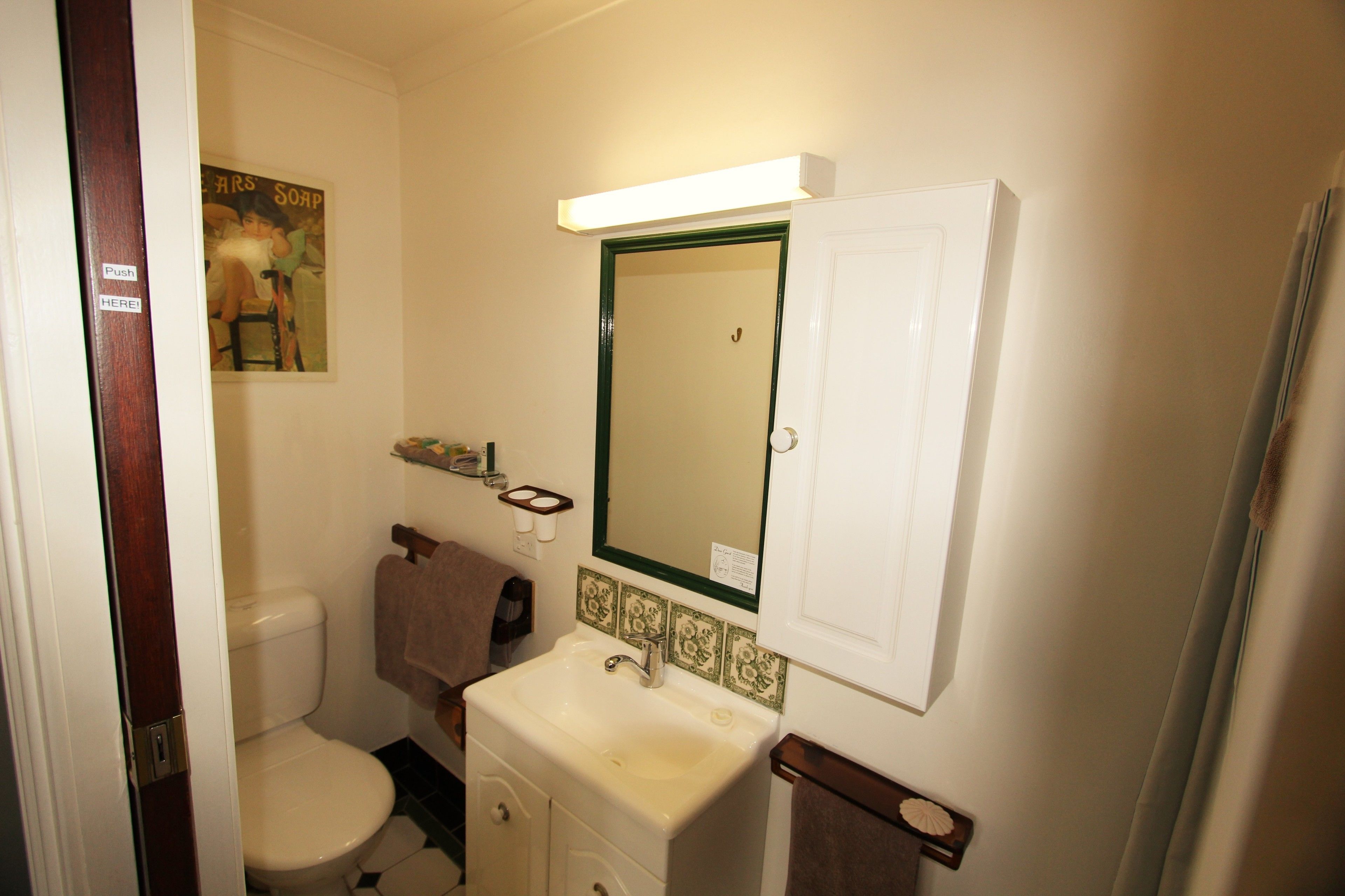 A bathroom with a toilet, sink, mirror, and towel rack.