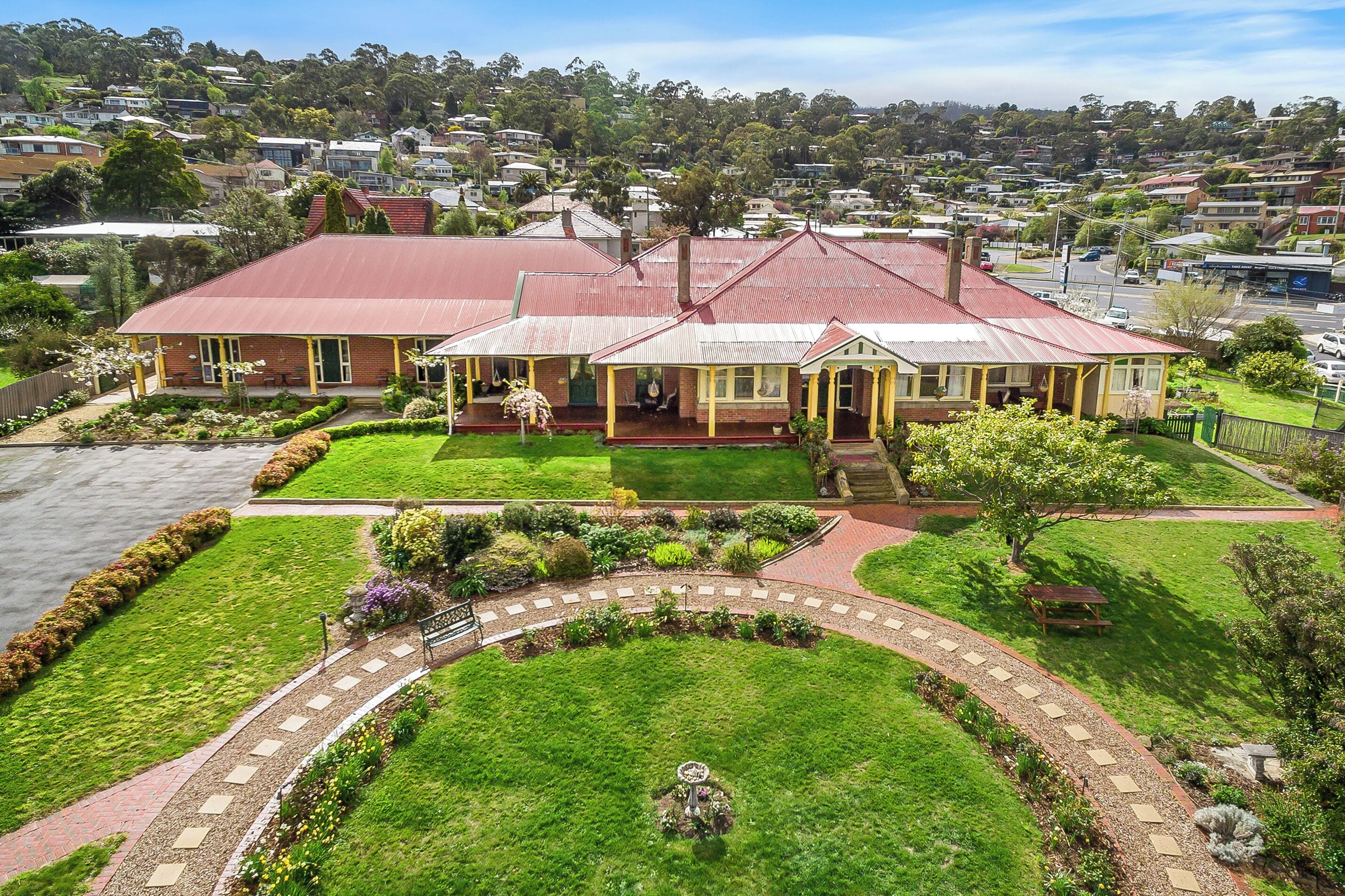A two-story house with a red roof, surrounded by a well-maintained garden and a paved driveway.