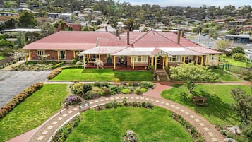 A two-story house with a red roof, surrounded by a well-maintained garden and a paved driveway.