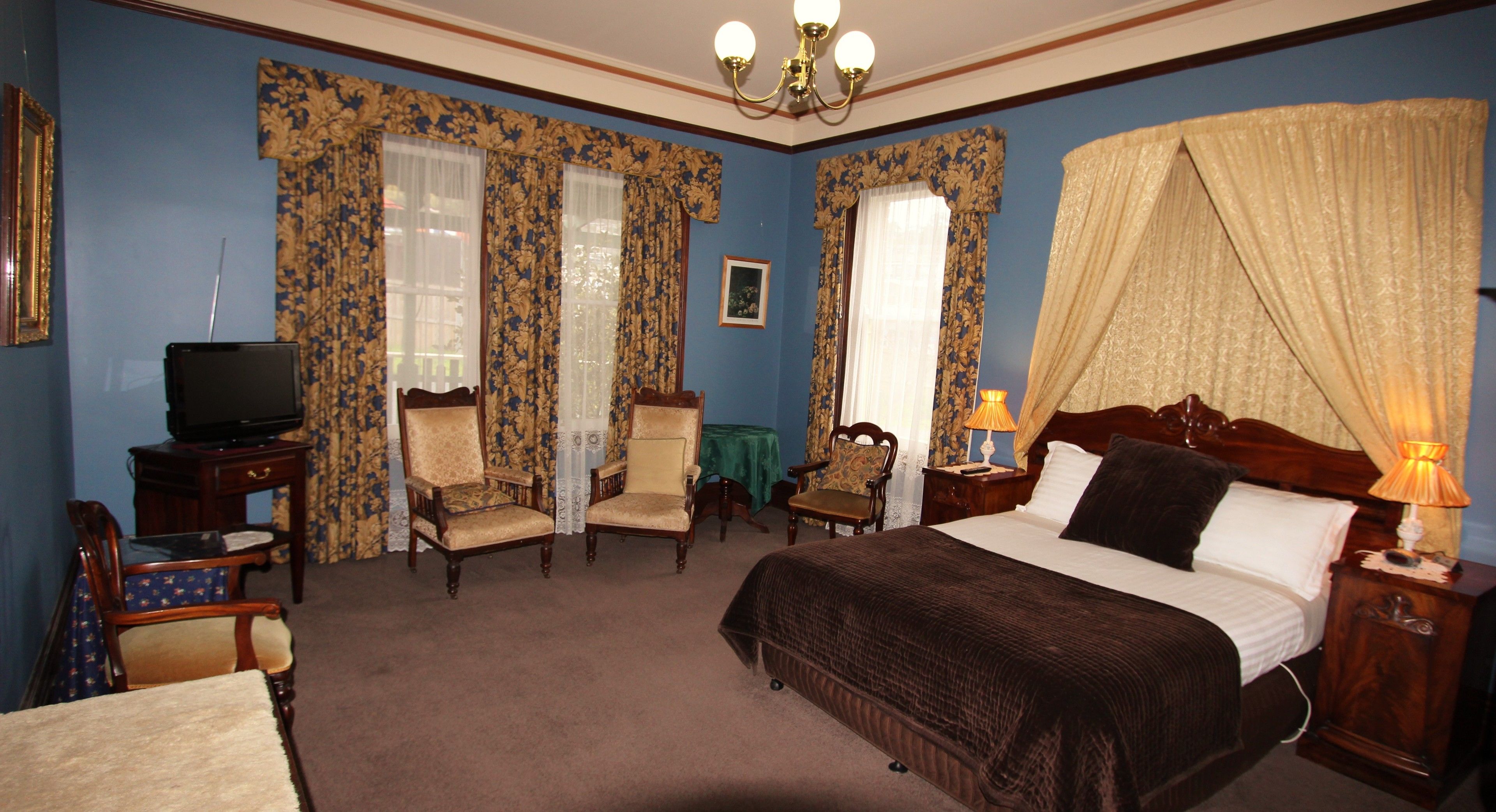 A hotel room with a bed, two armchairs, a small table, a television, and a nightstand with a lamp.