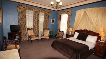 A hotel room with a bed, two armchairs, a small table, a television, and a nightstand with a lamp.