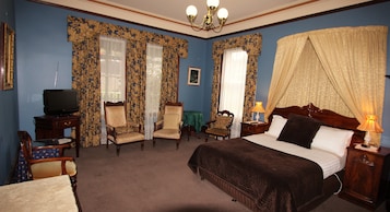 Habitación de hotel con cama, dos sillones, una mesita, televisión y mesita de noche con lámpara.