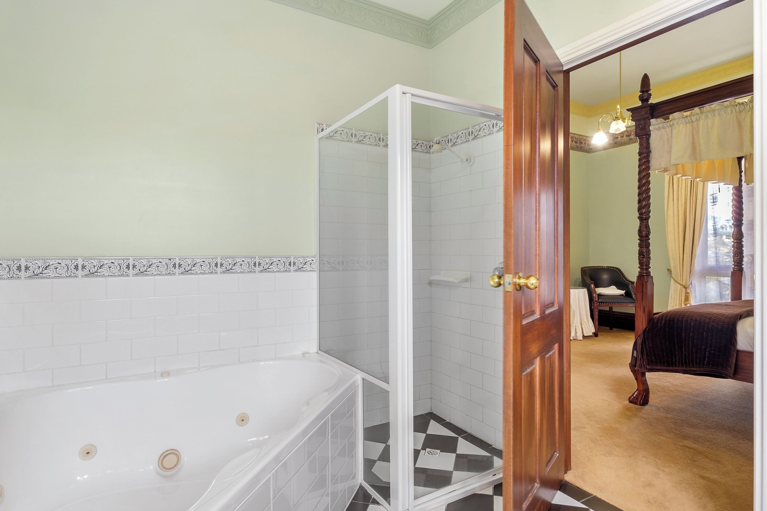 Un baño con bañera, ducha y una puerta que da a un dormitorio con cama con dosel.