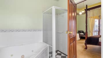 Un baño con bañera, ducha y una puerta que da a un dormitorio con cama con dosel.