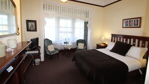 A hotel room with a large bed, a desk with a computer, a chair, a small table, and a window with curtains.