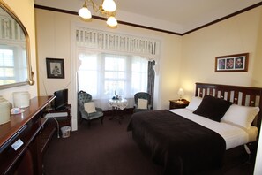 A hotel room with a large bed, a desk with a computer, a chair, a small table, and a window with curtains. - Orana House (Lindisfarne)