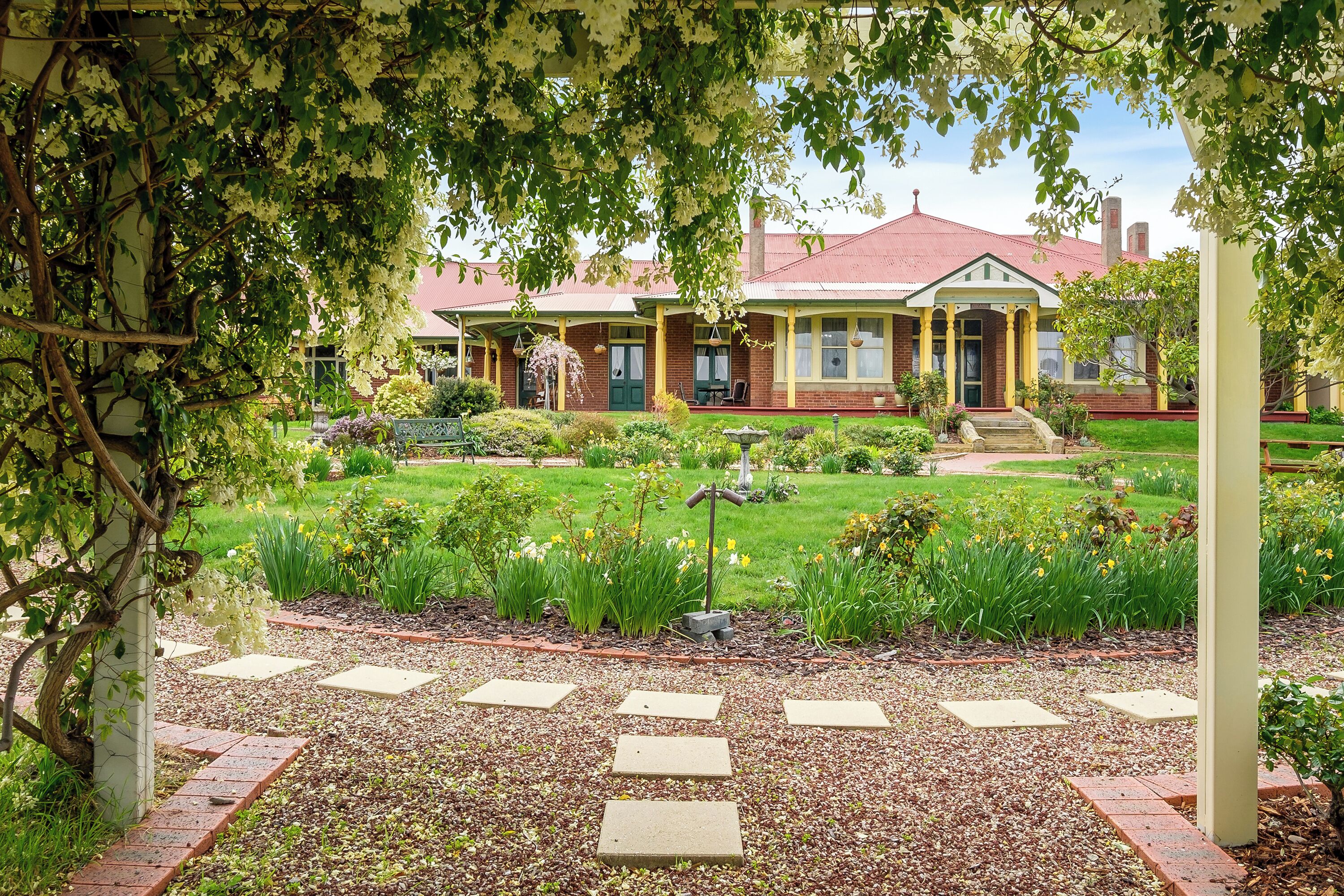 Una casa de ladrillo tradicional con techo rojo, rodeada por un jardín cuidado con diversas plantas y un sendero pavimentado.