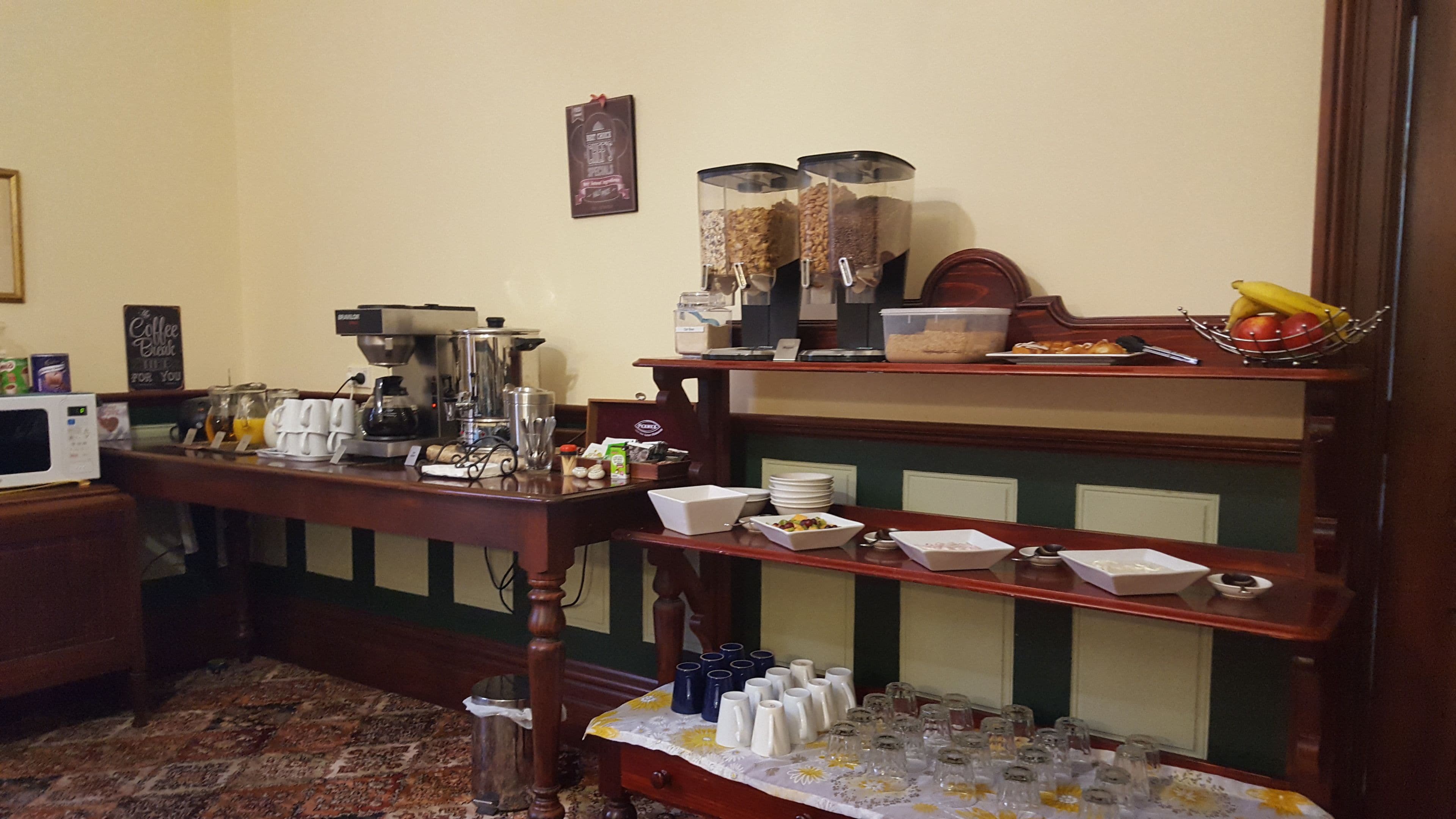 Una barra de desayuno con cafeteras, un frutero y diversas opciones para el desayuno.