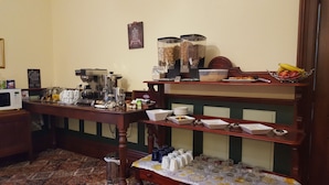 A breakfast bar with coffee machines, a fruit bowl, and various breakfast items.