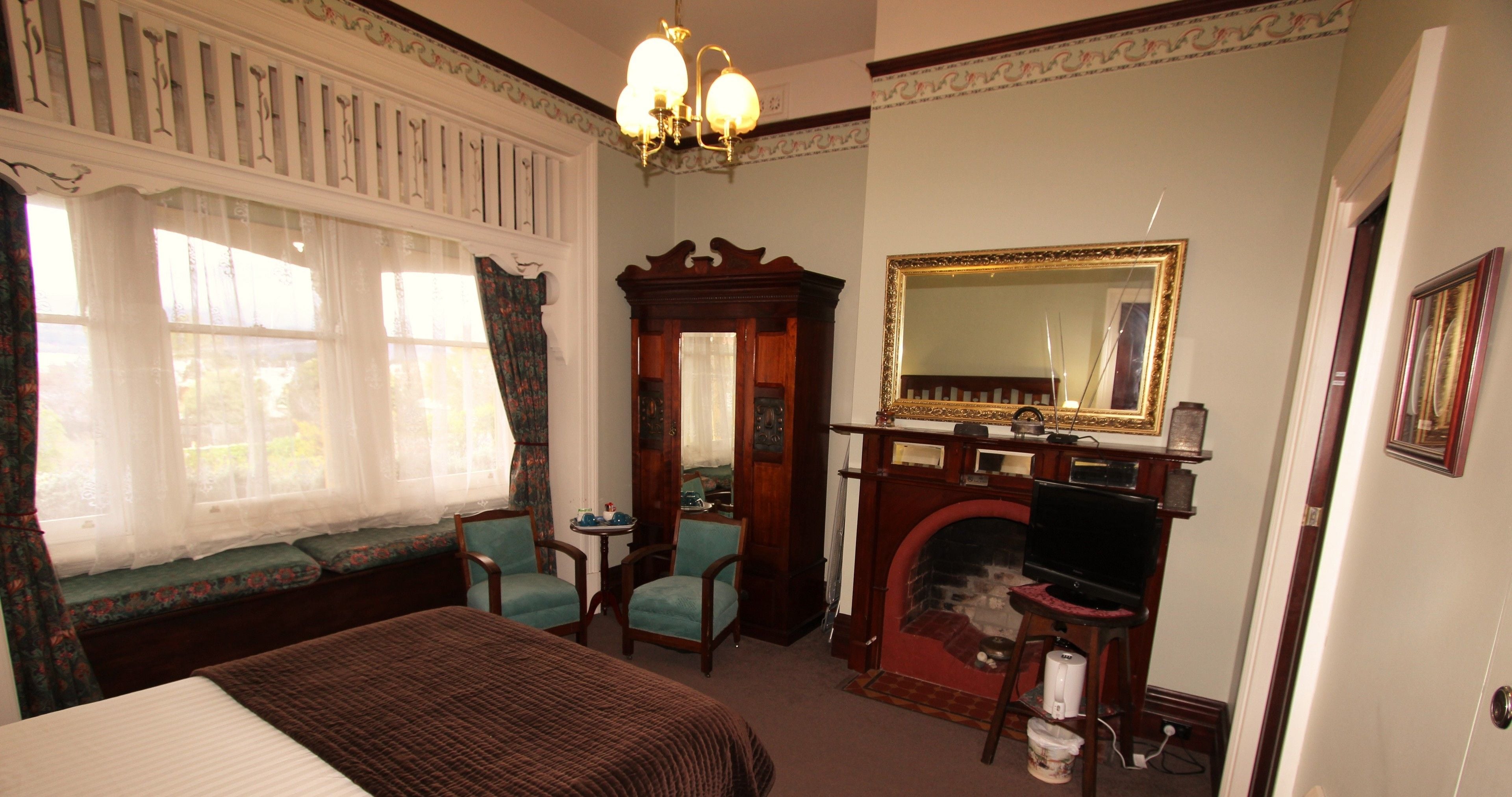 A bedroom with a large bed, two chairs, a fireplace, a television, and a mirror.