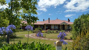 A two-story house with a red roof and yellow trim, surrounded by a well-maintained garden with purple flowers and a gravel pathway.