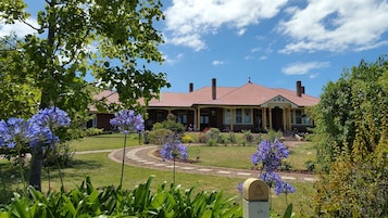 A two-story house with a red roof and yellow trim, surrounded by a well-maintained garden with purple flowers and a gravel pathway.
