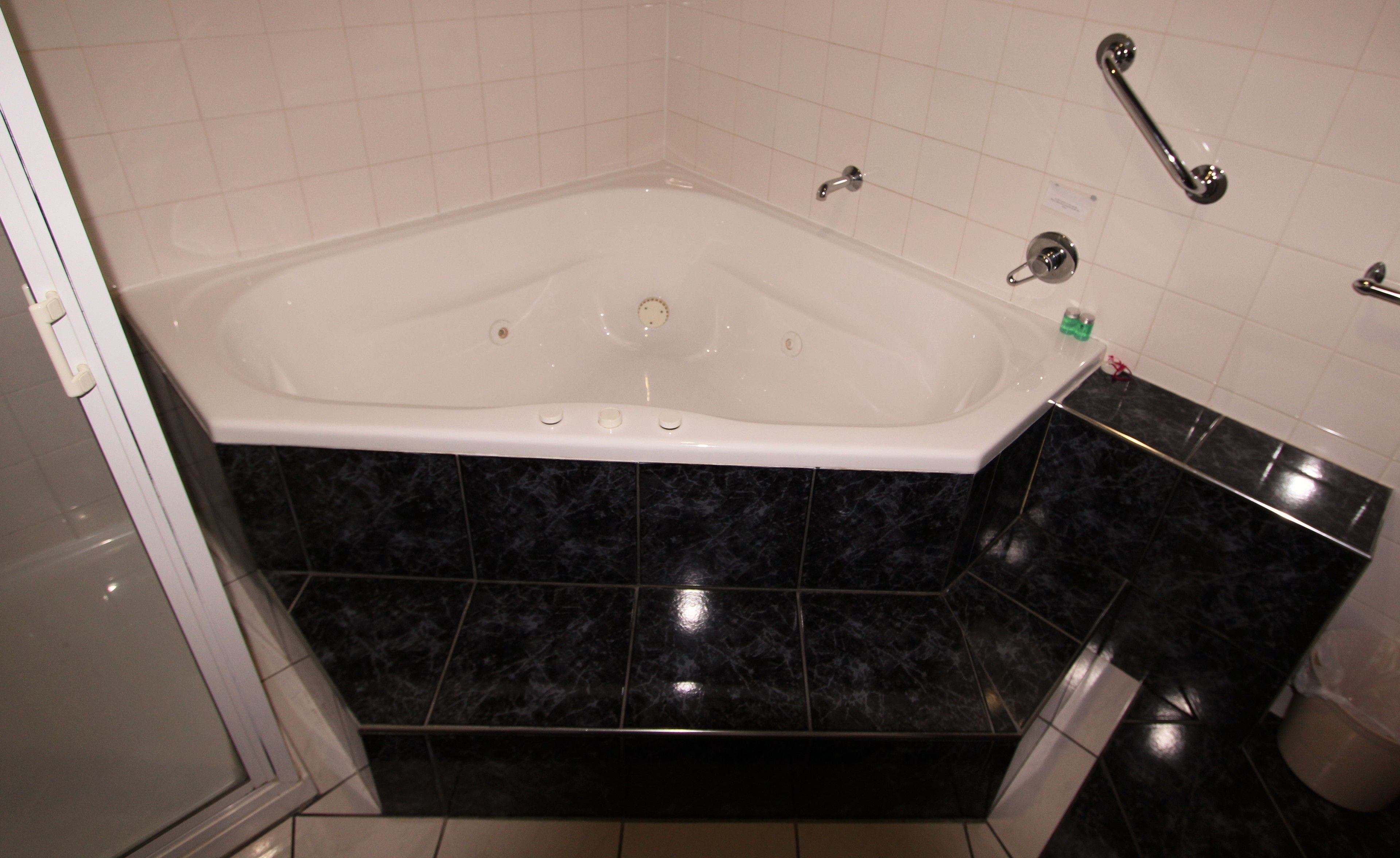 Un baño con una bañera blanca, baldosas de mármol negro, un lavamanos blanco y un pasamanos.