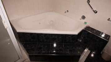Un baño con una bañera blanca, baldosas de mármol negro, un lavamanos blanco y un pasamanos.
