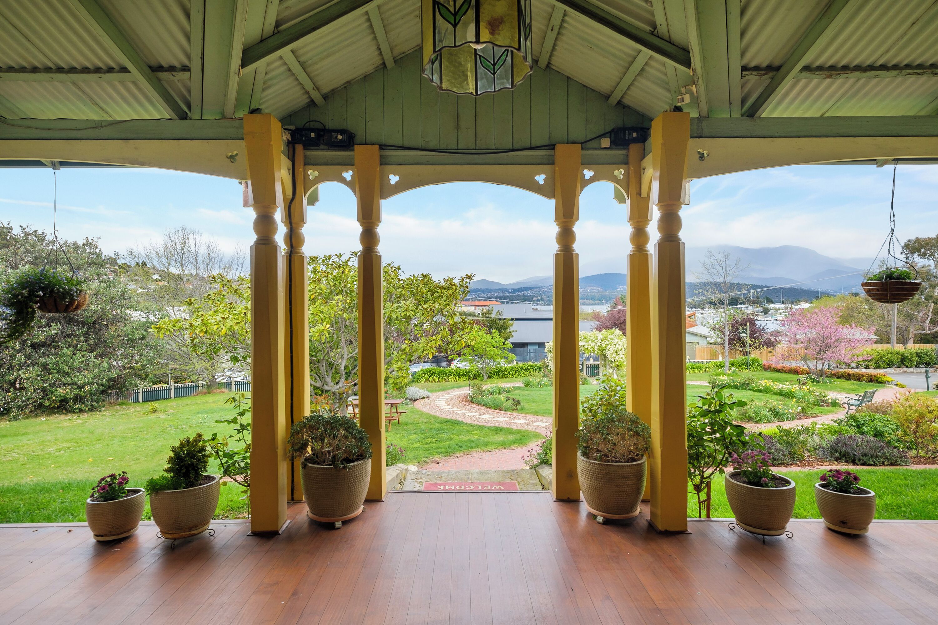 A covered outdoor area with a view of a garden and distant mountains.