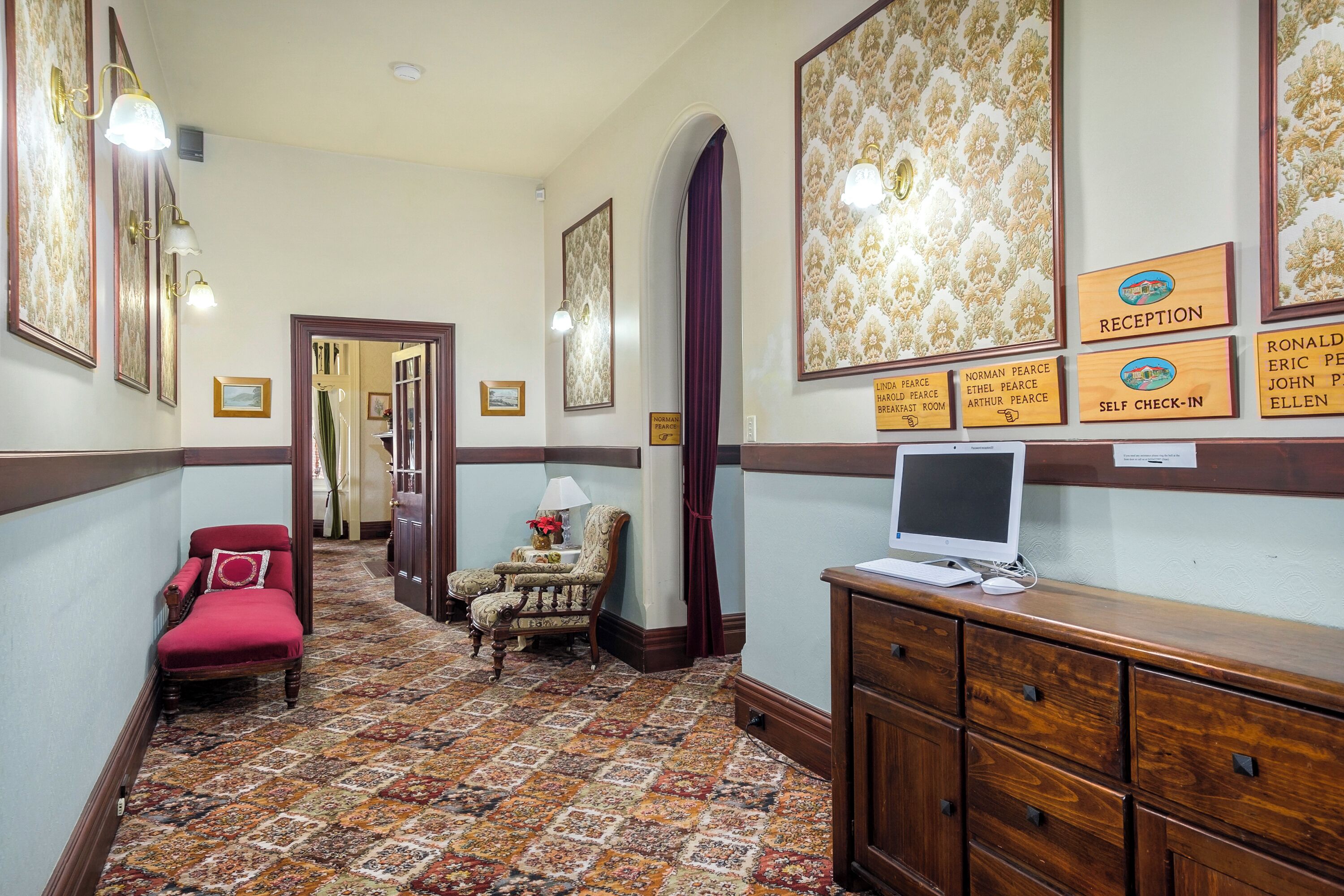 A hallway with a reception desk, a computer, a red chair, and a patterned carpet.