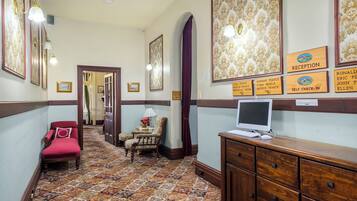 A hallway with a reception desk, a computer, a red chair, and a patterned carpet.