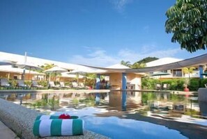 A pool area with lounge chairs and umbrellas, surrounded by greenery and buildings.