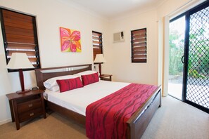 A bedroom with a bed, nightstands, a painting, and a view through a sliding door.