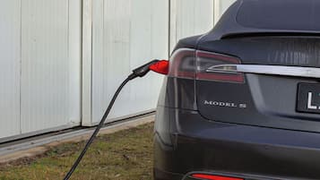 A car with a charging cable connected to it, parked in front of a white building.