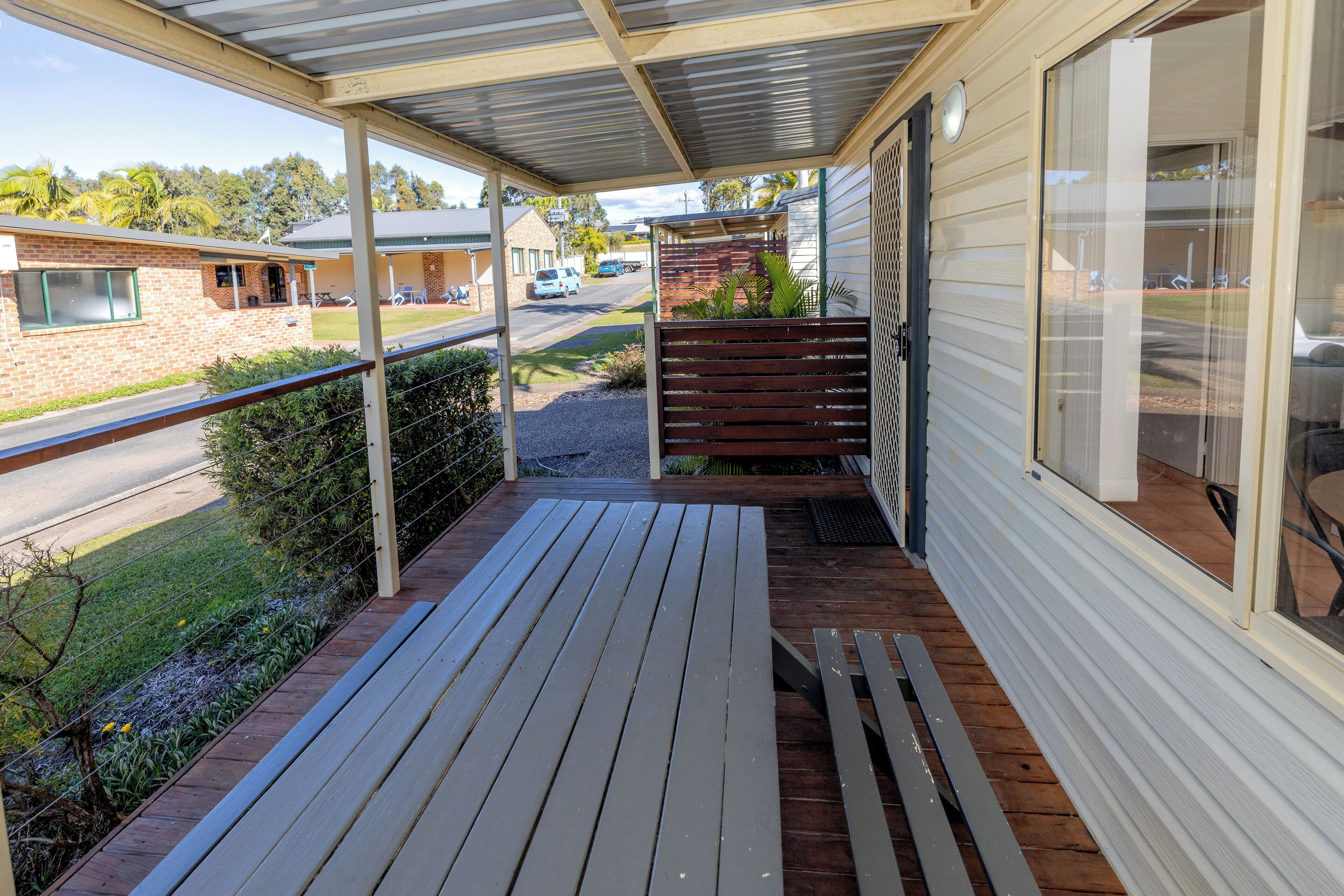 A covered porch with a wooden deck, a brick building in the background, and a clear view of the street.