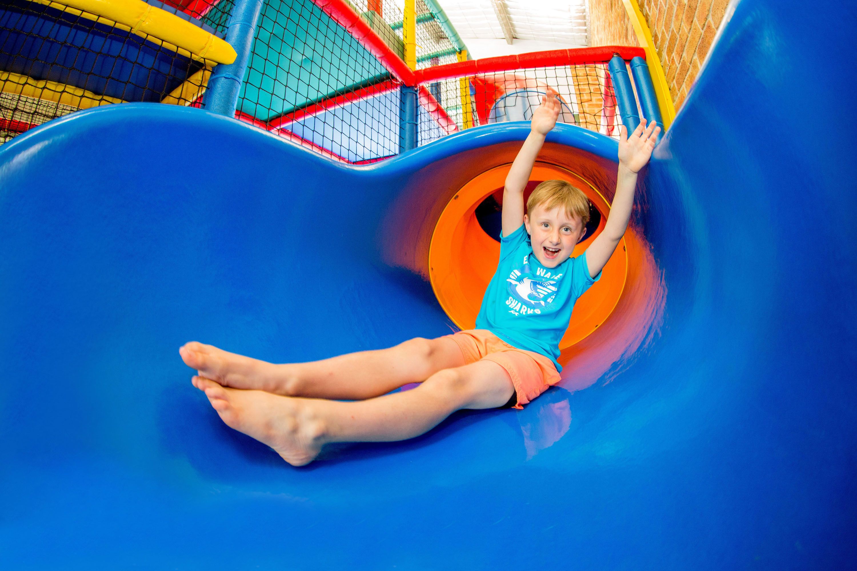 Un enfant glisse sur un toboggan bleu dans un parc.