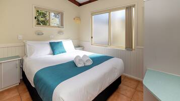 A neatly made bed with white and teal bedding, two bedside tables, and a window with curtains.
