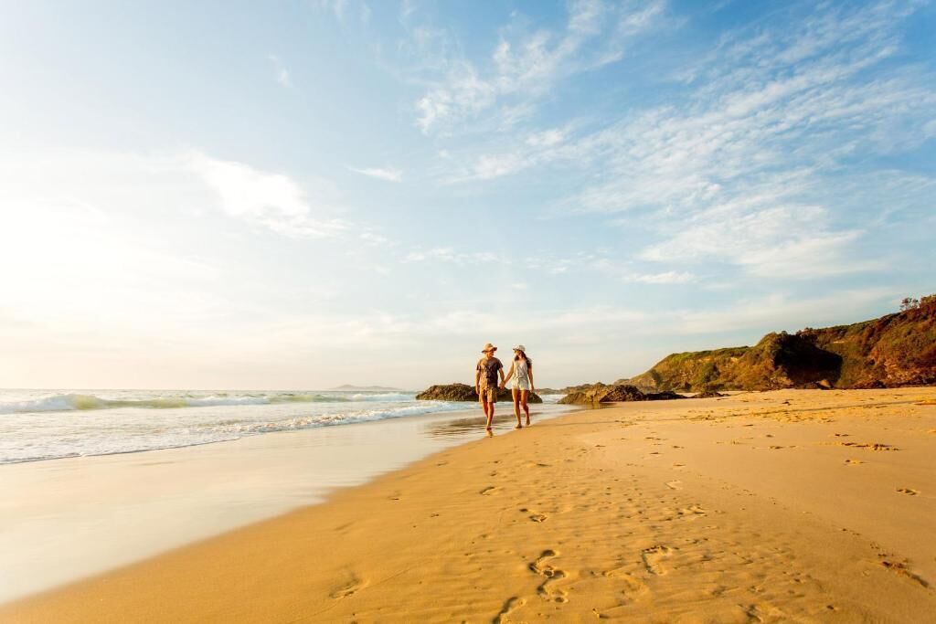 Ein Strand mit Fußabdrücken, die zum Wasser führen, Felsen und einem klaren Himmel.
